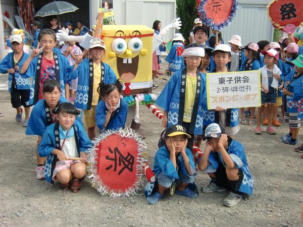 スポンジボブのキャラクターお神輿の前で法被を着た東子ども会の子供達が集まり一緒に記念撮影をしている写真